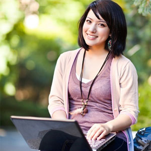 College student sitting on the ground with her computer in her lap.